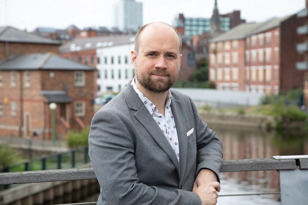 Photo of a white man in a jacket standing in front of a city scape