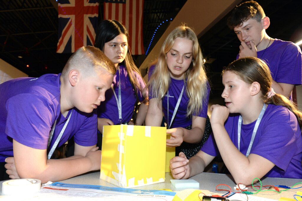 5 children in purple t shirts consider a yellow box model as part of an engineering project for the IET's Faraday Challenge