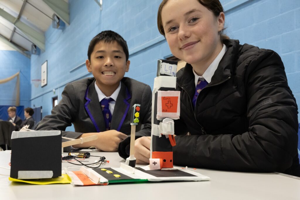A young girl and boy sit with a model of a traffic stopping system they created as part of the IET Faraday Challenge competition