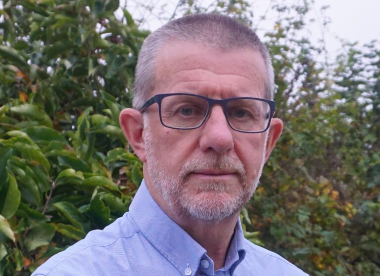 Head shot of white man with pale blue shirt with glasses and a beard
