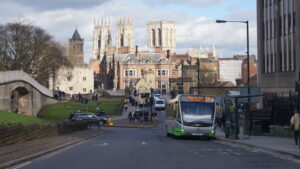 An image of a road junction in York, with a bus, cars and pedestrians in front of historic buildings.