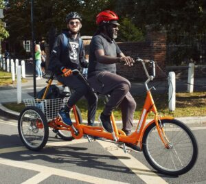 Two men sit on a three-wheeled Tandem bike